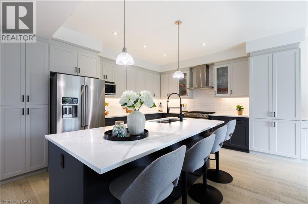 Modern kitchen featuring a large island with a substantial white countertop, light gray upper cabinetry, two-tone lower cabinetry, stainless steel appliances, and wood-finish flooring - 581 Doonwoods Crescent, Kitchener, ON - Indoor Photo Showing Kitchen With Stainless Steel Kitchen With Upgraded Kitchen
