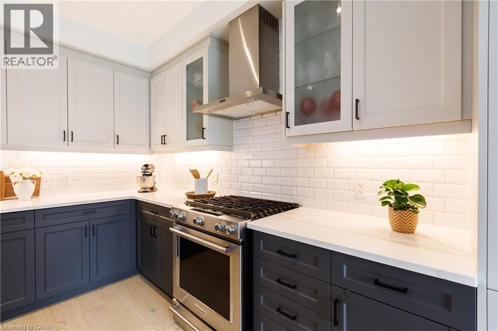 Contemporary kitchen featuring two-tone cabinetry, a stainless steel gas range with a matching range hood, white subway tile backsplash, white countertops, and under-cabinet lighting - 581 Doonwoods Crescent, Kitchener, ON - Indoor Photo Showing Kitchen With Upgraded Kitchen