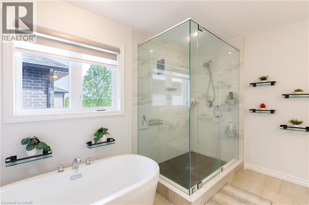 Contemporary bathroom featuring a freestanding soaking tub with deck-mounted chrome fixtures, a corner glass-enclosed shower with stone-look tile surround, and light-toned floor tile - 581 Doonwoods Crescent, Kitchener, ON - Indoor Photo Showing Bathroom