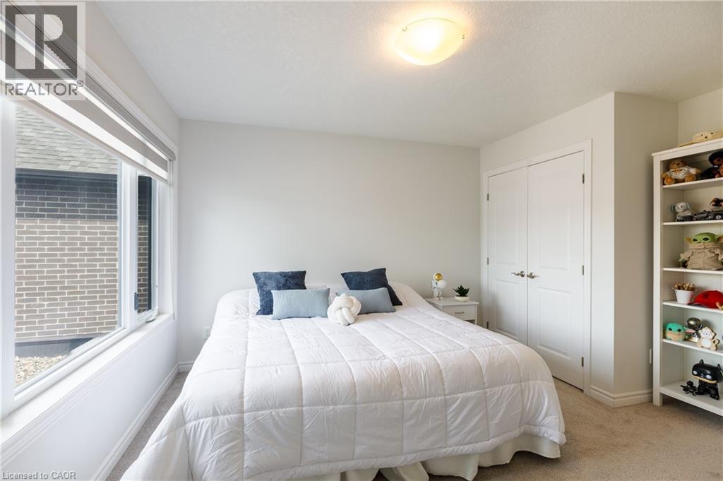 Carpeted bedroom with a large window featuring blinds, a ceiling-mounted light fixture, and double bi-fold closet doors - 581 Doonwoods Crescent, Kitchener, ON - Indoor Photo Showing Bedroom