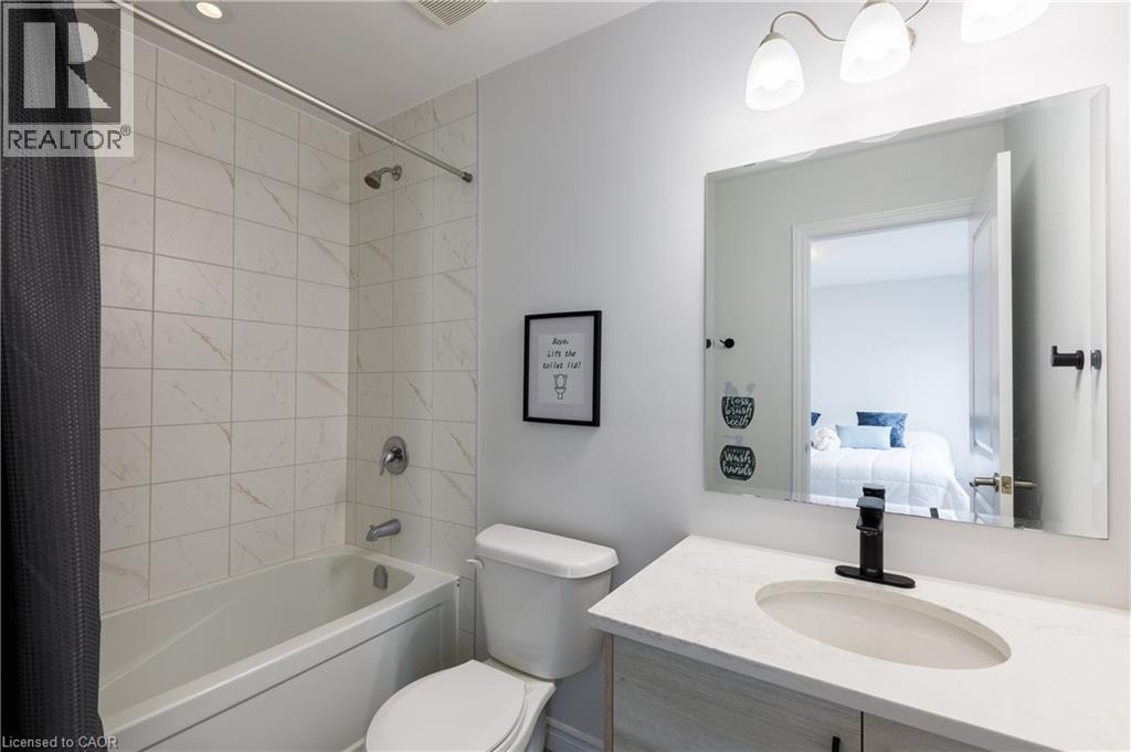 Bathroom with a white tiled shower and tub combination, a toilet, and a vanity featuring a matte black faucet and an oval undermount sink set into a light-toned countertop - 581 Doonwoods Crescent, Kitchener, ON - Indoor Photo Showing Bathroom
