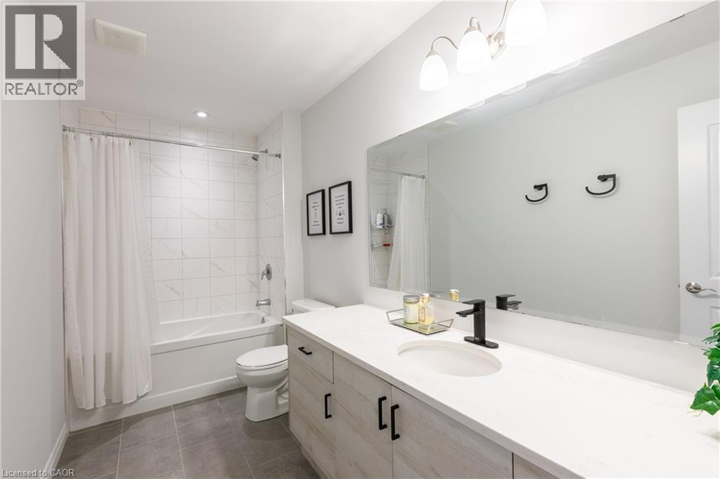 Bathroom featuring a white bathtub and shower with tile surround, a single vanity with an integrated sink, a large wall-mounted mirror, and gray tile flooring - 581 Doonwoods Crescent, Kitchener, ON - Indoor Photo Showing Bathroom