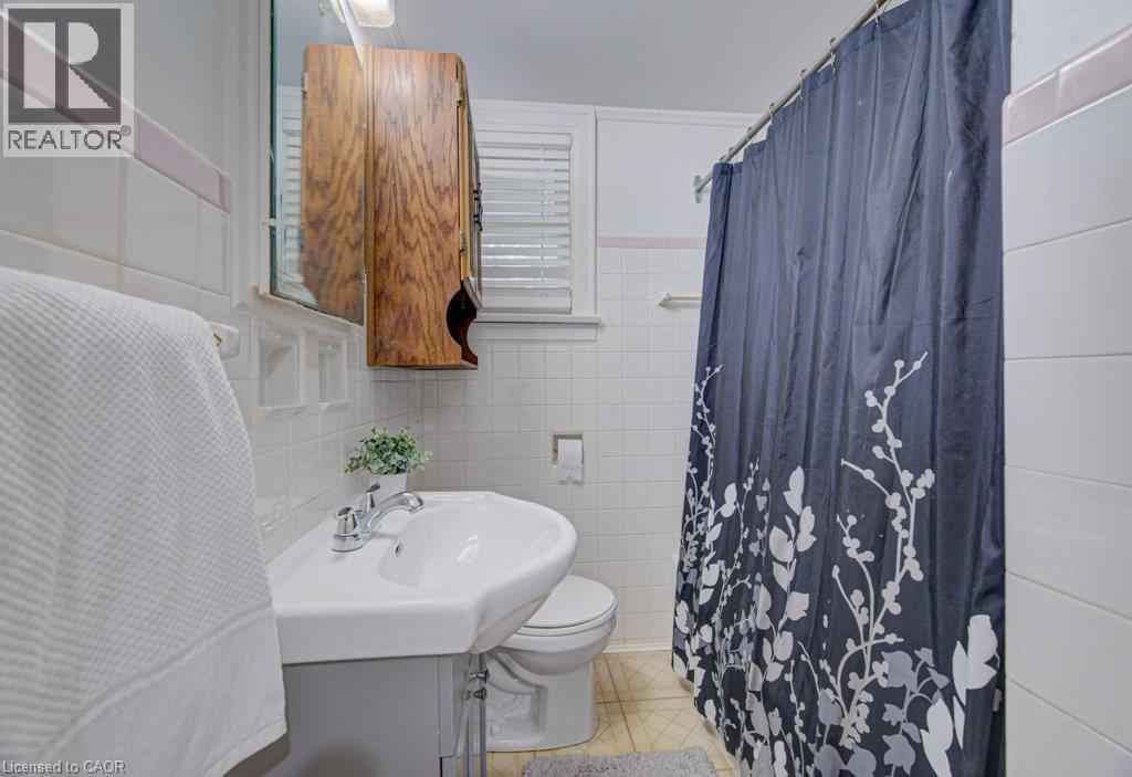 Bathroom featuring a pedestal sink with chrome faucet, a wall-mounted wooden cabinet, and white tiled walls with a pink accent stripe - 128 Pollock Avenue, Cambridge, ON - Indoor Photo Showing Bathroom