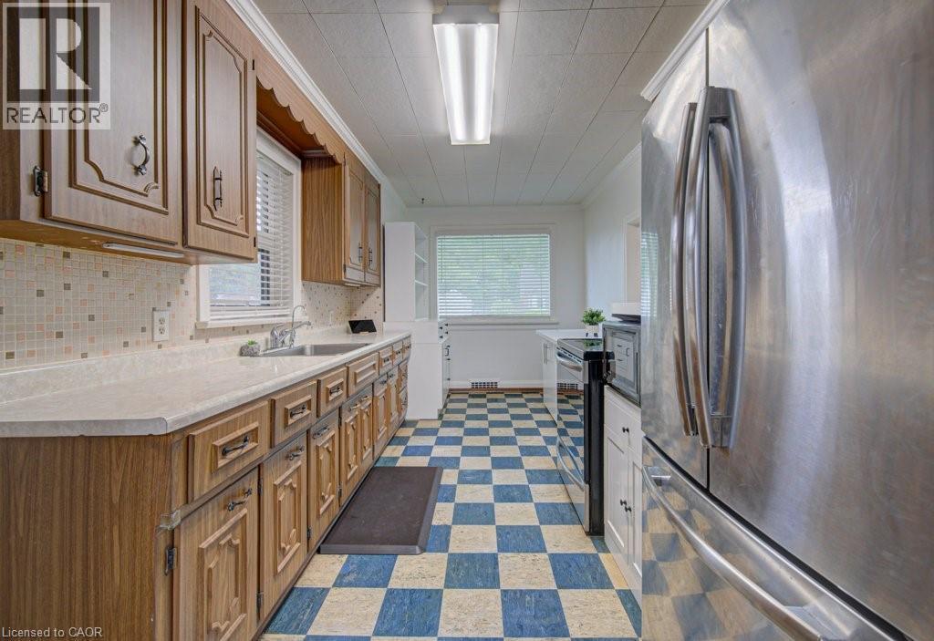 Kitchen featuring extensive wood-finish cabinetry, light-toned countertops, a mosaic tile backsplash, stainless steel refrigerator, and checkerboard floor tiling - 128 Pollock Avenue, Cambridge, ON - Indoor Photo Showing Kitchen