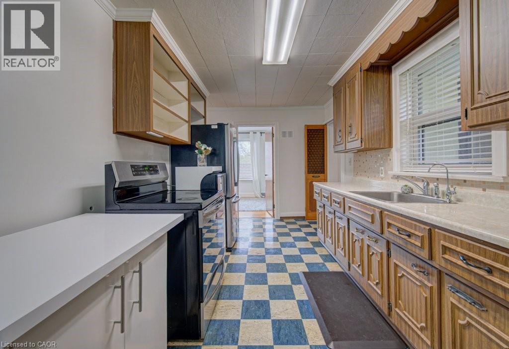 Galley kitchen featuring wood-finish cabinetry, a stainless steel sink, and a black electric range - 128 Pollock Avenue, Cambridge, ON - Indoor Photo Showing Kitchen