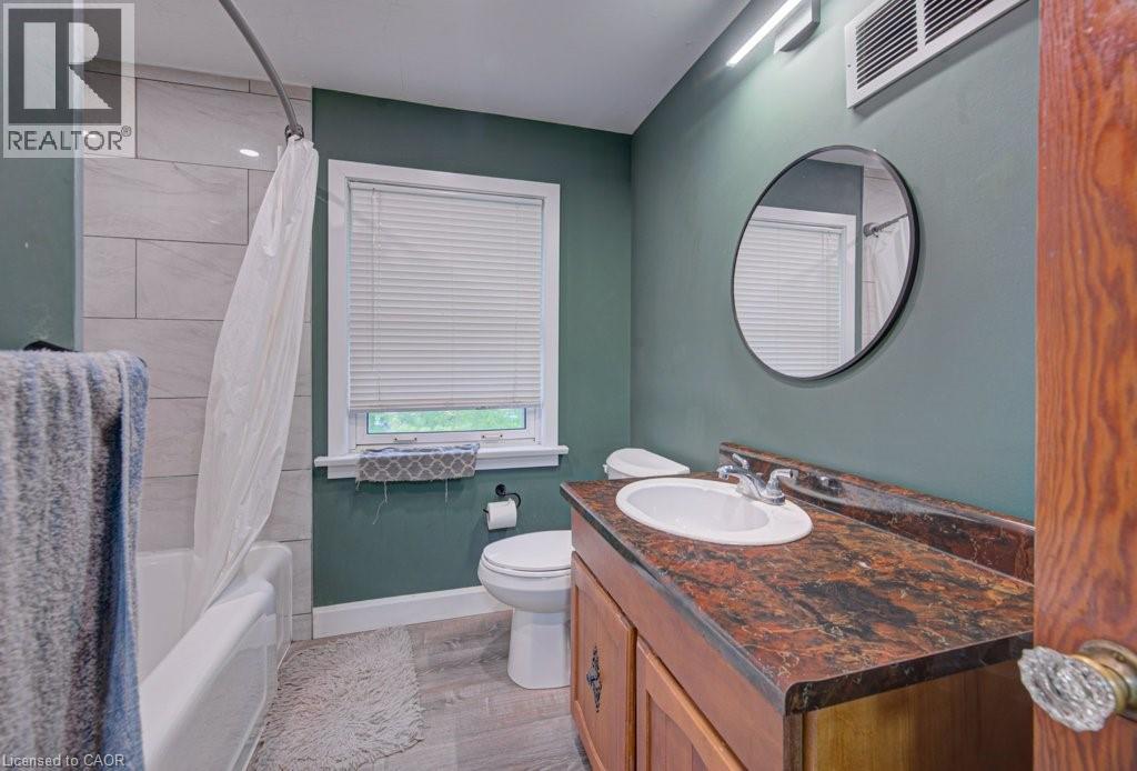 Bathroom featuring a wood-finish vanity with an integrated sink, a dark speckled countertop, and a round wall-mounted mirror - 128 Pollock Avenue, Cambridge, ON - Indoor Photo Showing Bathroom
