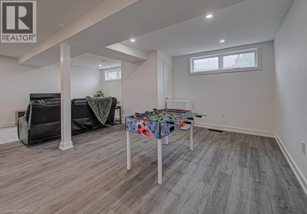 Spacious recreation room featuring wood-finish flooring, recessed lighting, and white baseboards - 128 Pollock Avenue, Cambridge, ON - Indoor