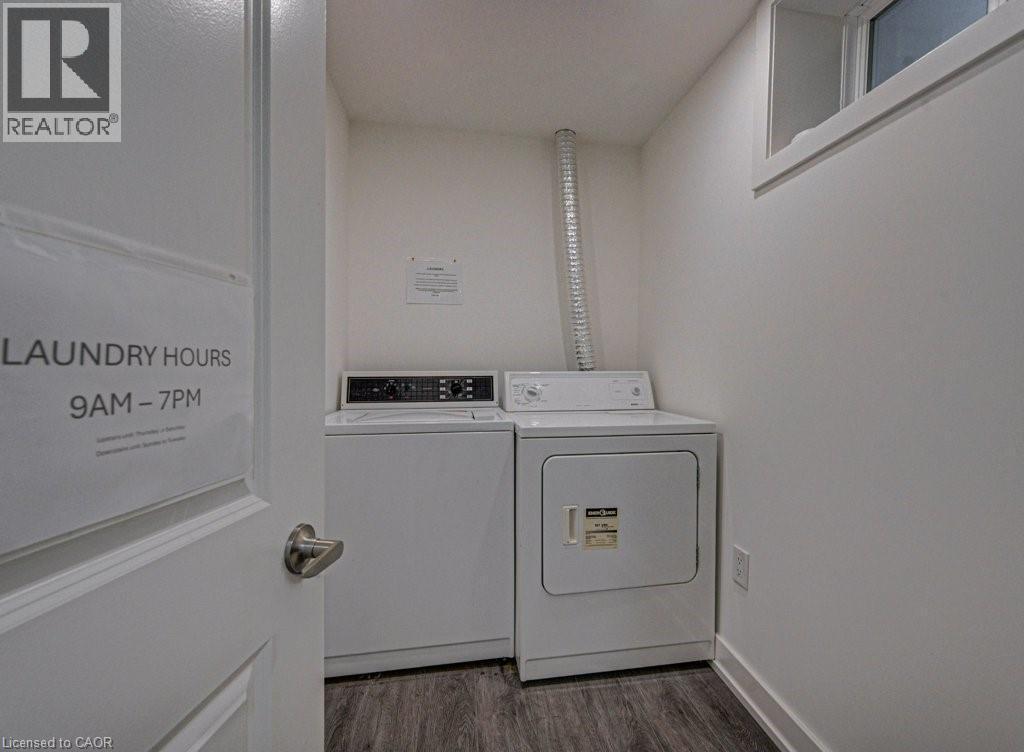 Dedicated laundry area featuring a white washer and dryer pair, wood-finish flooring, and an elevated window - 128 Pollock Avenue, Cambridge, ON - Indoor Photo Showing Laundry Room