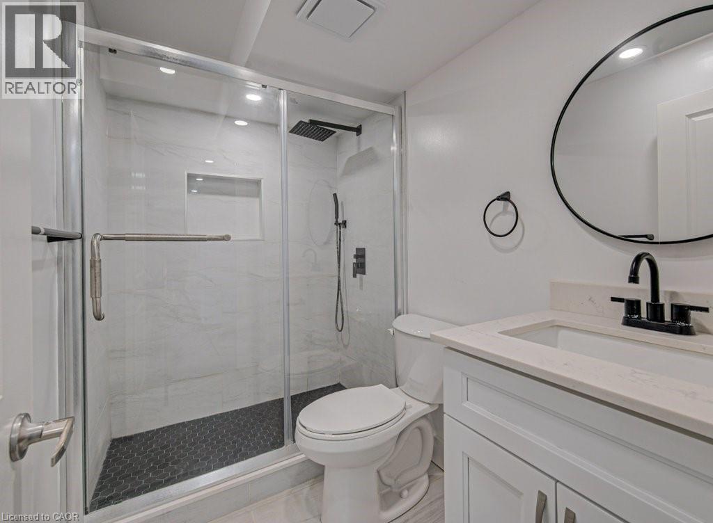 Contemporary bathroom featuring a frameless glass shower enclosure with white tile surround, a dark hexagonal tile shower floor, and a built-in shower niche - 128 Pollock Avenue, Cambridge, ON - Indoor Photo Showing Bathroom