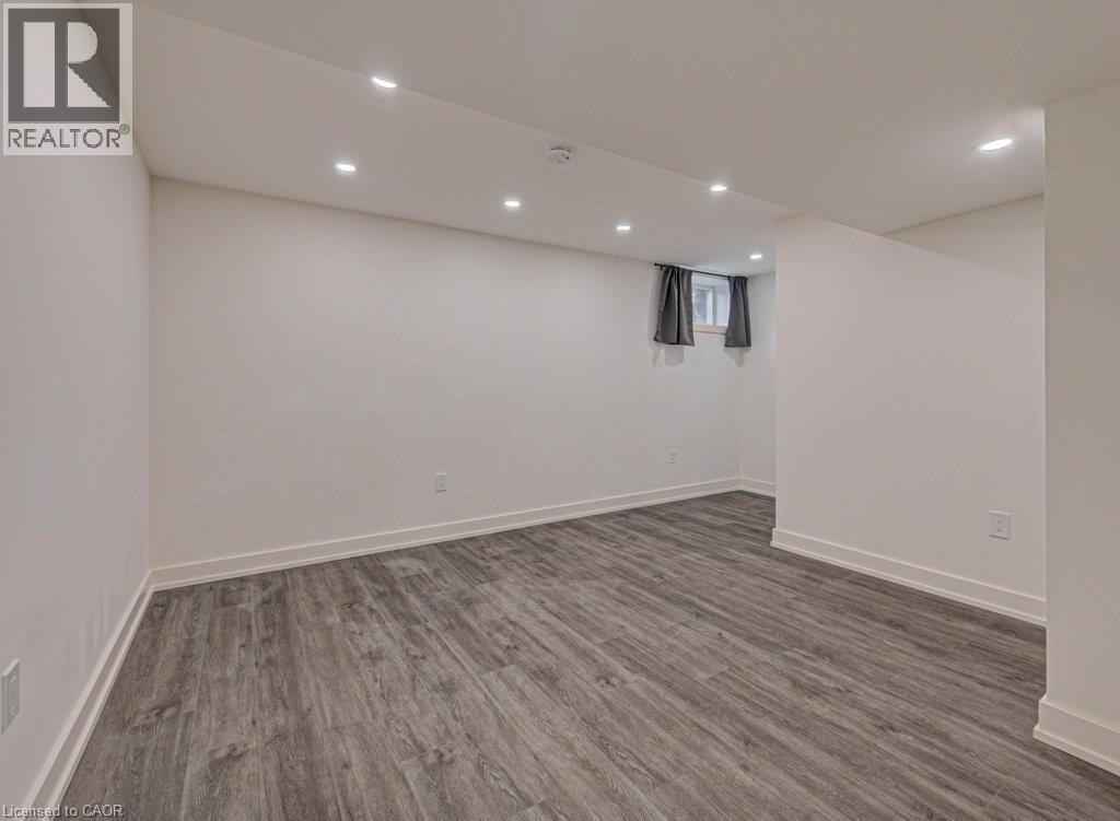 Finished lower-level space featuring contemporary wood-finish flooring, recessed ceiling lighting, and white baseboards - 128 Pollock Avenue, Cambridge, ON - Indoor
