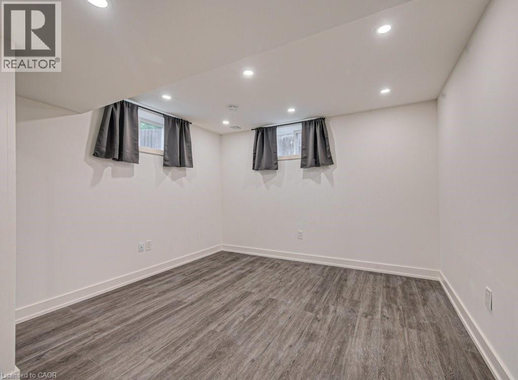 Spacious room featuring wood-finish flooring, white walls, recessed ceiling lighting, and two windows with drapery - 128 Pollock Avenue, Cambridge, ON - Indoor Photo Showing Other Room