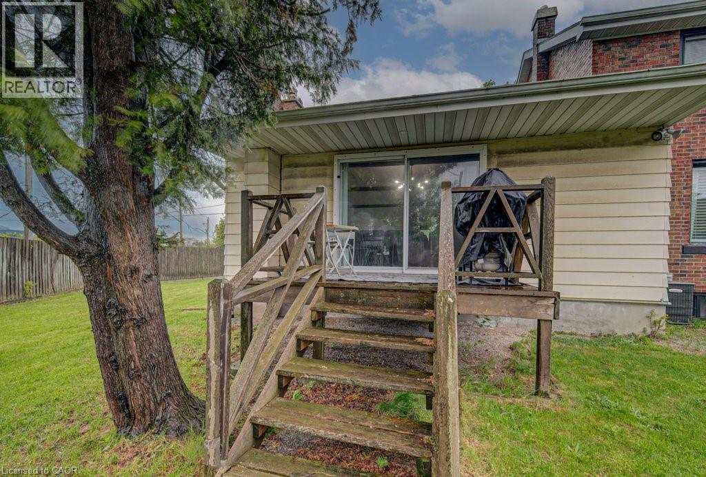 Rear exterior featuring a wooden deck with railing, sliding glass door, and a mature tree - 128 Pollock Avenue, Cambridge, ON - Outdoor