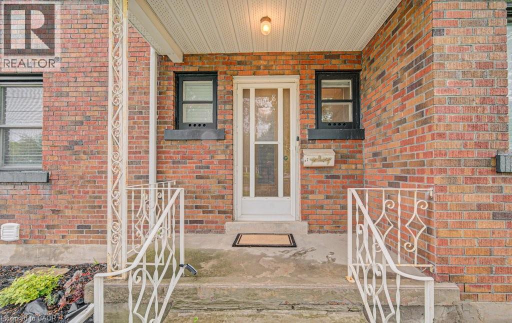Brick exterior featuring a covered entryway with a white screen door, decorative metal railings, and an overhead light fixture - 128 Pollock Avenue, Cambridge, ON - Outdoor With Exterior