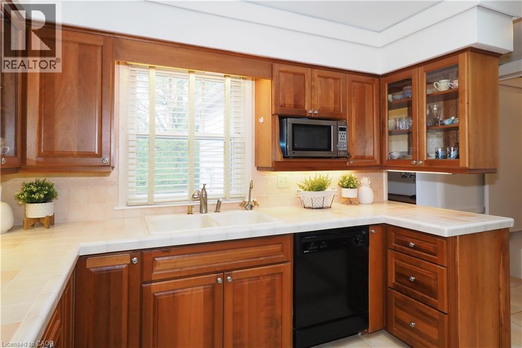 Kitchen featuring wood cabinetry, light-toned countertops, a double basin sink with a brushed nickel faucet, a built-in microwave, and an integrated dishwasher - 2023 Coronation Boulevard, Cambridge, ON - Indoor Photo Showing Kitchen With Double Sink