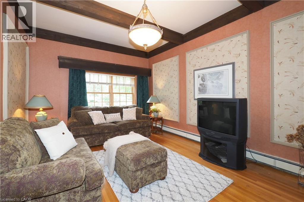 Living area featuring exposed ceiling beams, wood-finish flooring, a multi-pane window, and wall panels with decorative trim - 2023 Coronation Boulevard, Cambridge, ON - Indoor Photo Showing Living Room