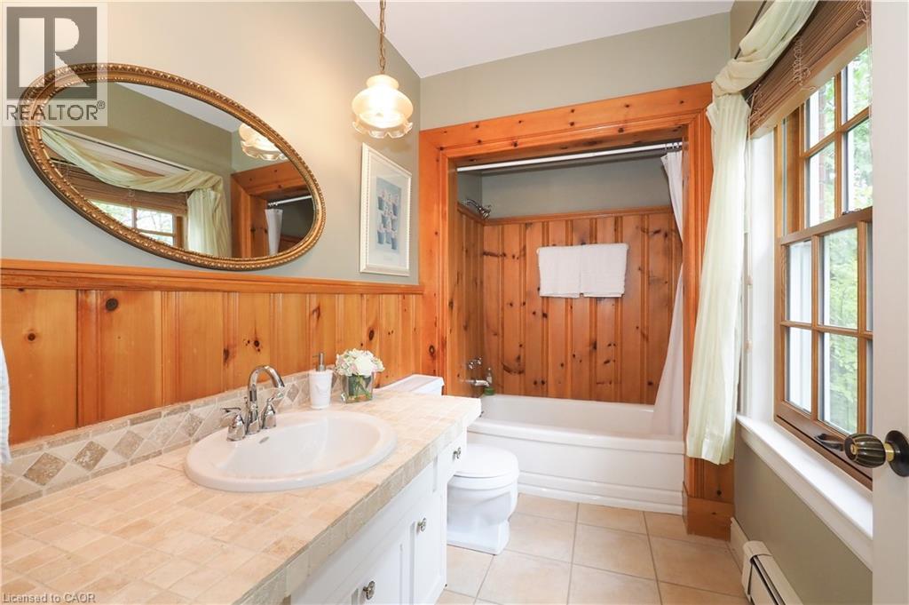 Bathroom featuring wood-paneled walls, a tile countertop with an integrated sink, and an oval mirror - 2023 Coronation Boulevard, Cambridge, ON - Indoor Photo Showing Bathroom