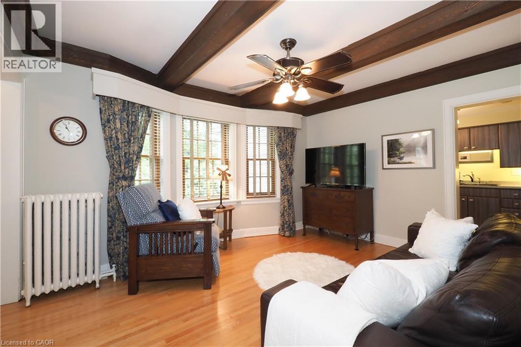 Living area featuring wood-finish flooring, exposed ceiling beams, a bay window with natural light, a ceiling fan, and a radiator - 2023 Coronation Boulevard, Cambridge, ON - Indoor Photo Showing Living Room