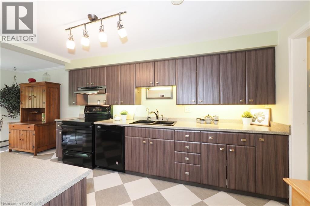 Kitchen featuring wood-finish cabinetry, black appliances, track lighting, light-toned countertops, and checkerboard flooring - 2023 Coronation Boulevard, Cambridge, ON - Indoor Photo Showing Kitchen With Double Sink
