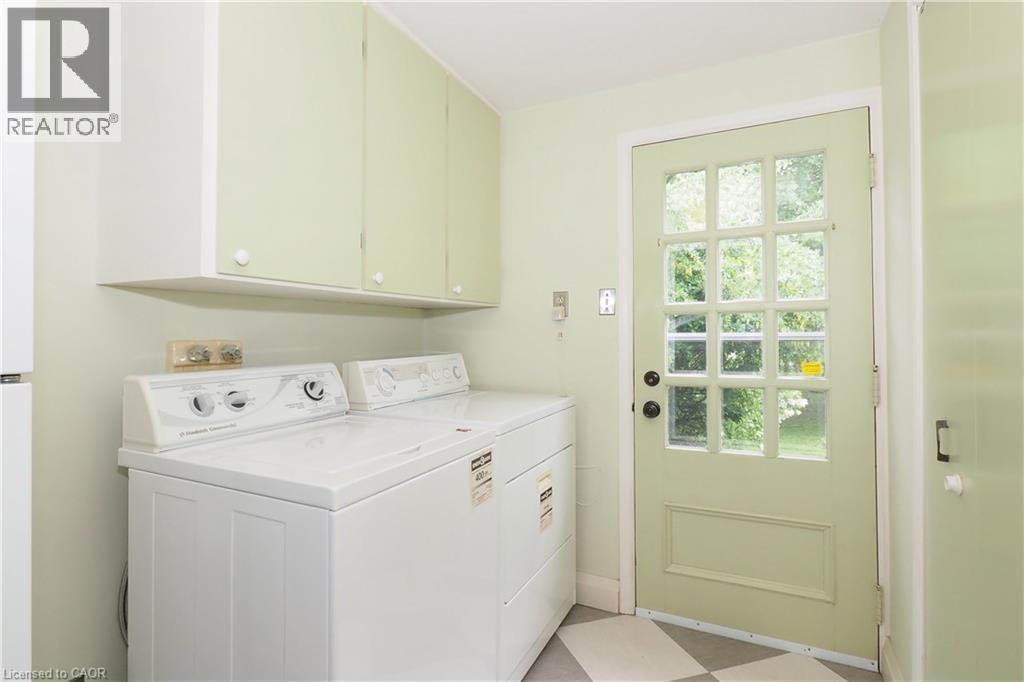 Dedicated laundry area featuring overhead cabinetry, a paneled exterior door with multiple glass lites, and checkerboard floor tiles - 2023 Coronation Boulevard, Cambridge, ON - Indoor Photo Showing Laundry Room