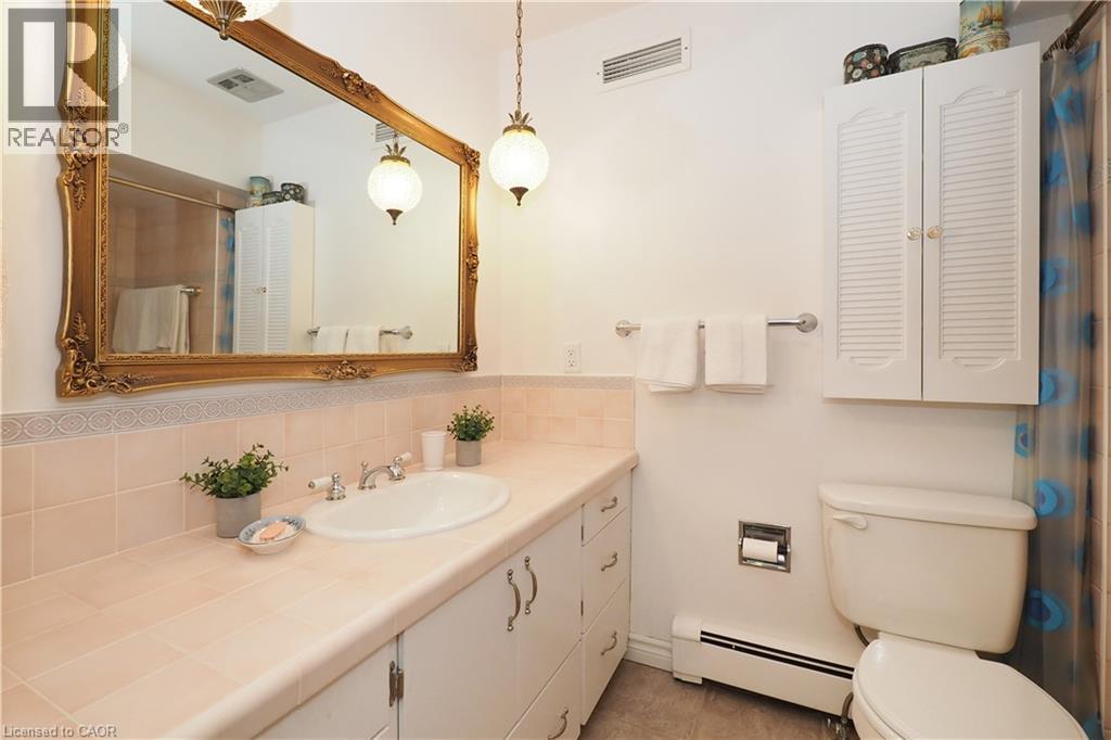 Bathroom vanity with an integrated basin, a large ornate gold-framed mirror, and two hanging pendant light fixtures - 2023 Coronation Boulevard, Cambridge, ON - Indoor Photo Showing Bathroom