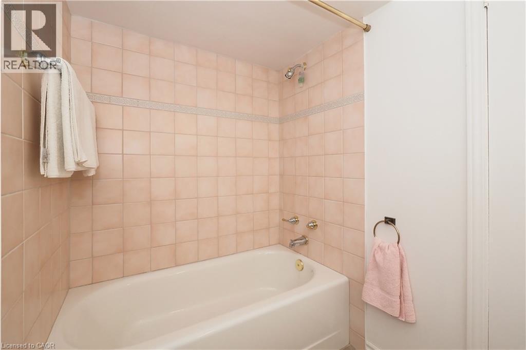 Bathroom featuring a standard bathtub with shower, light-toned square wall tiles, a decorative accent tile band, and polished chrome fixtures - 2023 Coronation Boulevard, Cambridge, ON - Indoor Photo Showing Bathroom