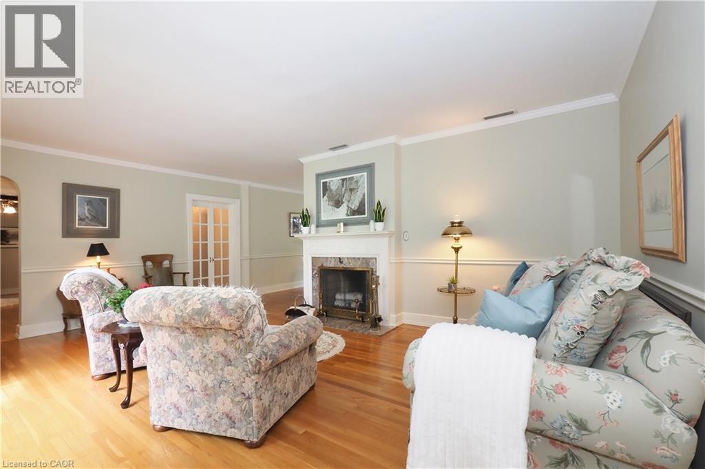 Living space featuring a fireplace with a white mantel, wood-finish flooring, white crown molding, and wainscoting - 2023 Coronation Boulevard, Cambridge, ON - Indoor Photo Showing Living Room With Fireplace