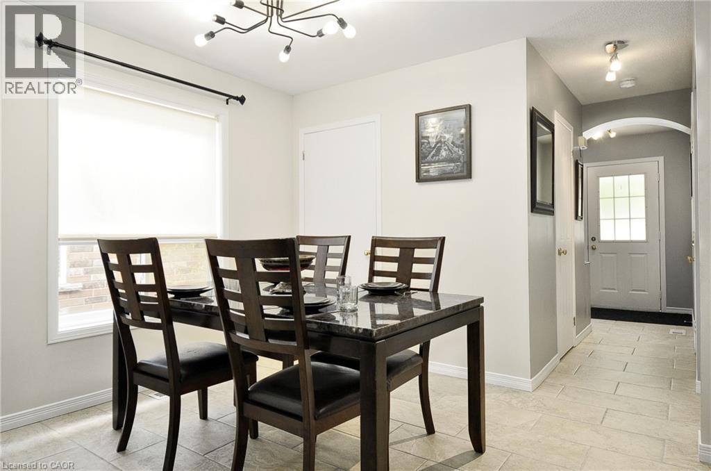 Dining area featuring a contemporary chandelier, a large window, light-toned tile flooring, and an arched entryway to the foyer - 12 Karalee Crescent, Cambridge, ON - Indoor Photo Showing Dining Room