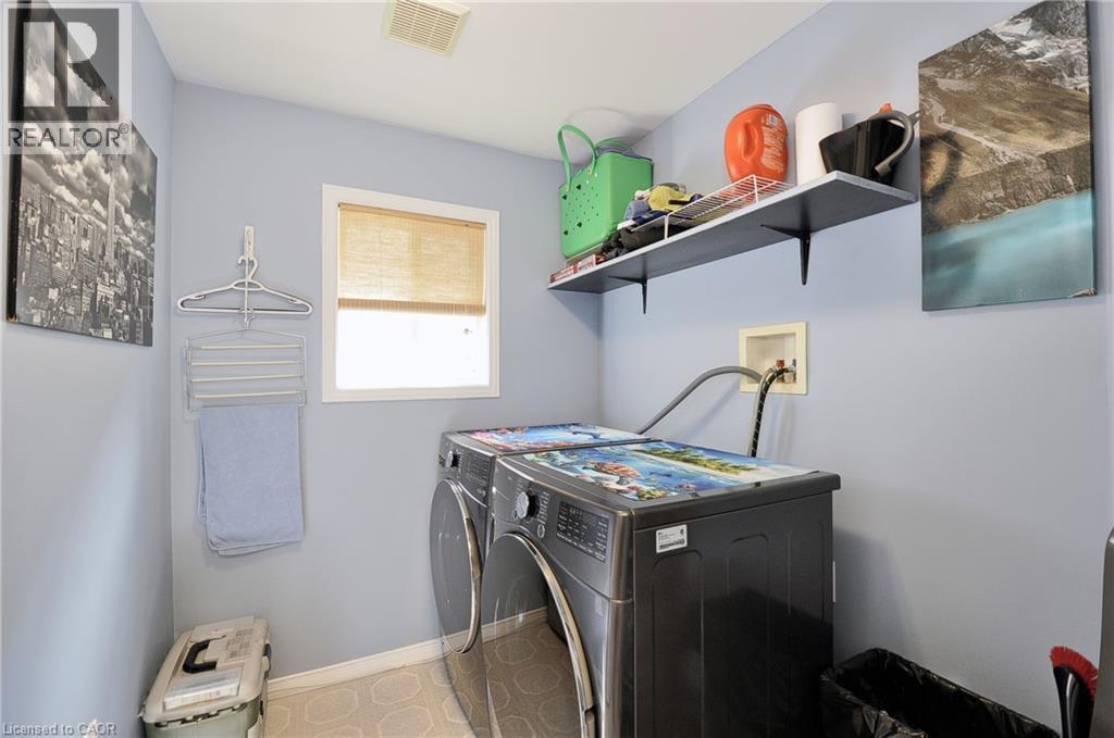 Dedicated laundry area featuring front-loading appliances, a built-in shelf with wall-mounted brackets, and a window with a natural fiber shade - 12 Karalee Crescent, Cambridge, ON - Indoor Photo Showing Laundry Room