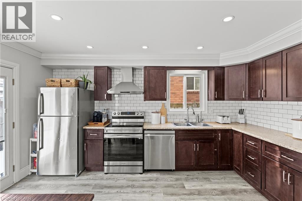 Kitchen with dark wood cabinetry, light-toned countertops, and a white subway tile backsplash - 27 Barbara Court, Hamilton, ON - Indoor Photo Showing Kitchen With Double Sink