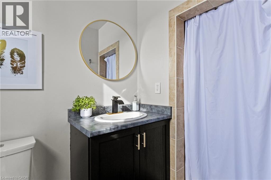 Bathroom vanity featuring a dark wood-finish cabinet with brass-tone hardware, a stone-finish countertop, and an undermount sink - 27 Barbara Court, Hamilton, ON - Indoor Photo Showing Bathroom