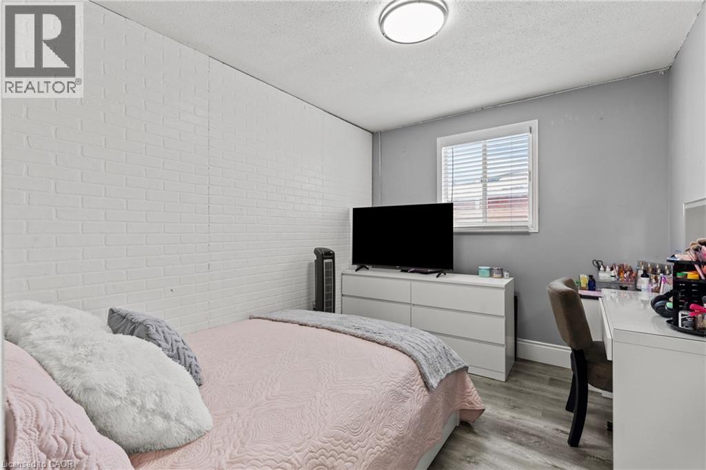 Bedroom featuring wood-finish flooring, a white faux brick accent wall, and a window with horizontal blinds - 27 Barbara Court, Hamilton, ON - Indoor Photo Showing Bedroom