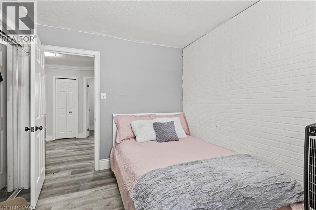 Room featuring wood-finish flooring, a white brick-patterned accent wall, and light gray painted walls - 27 Barbara Court, Hamilton, ON - Indoor Photo Showing Bedroom