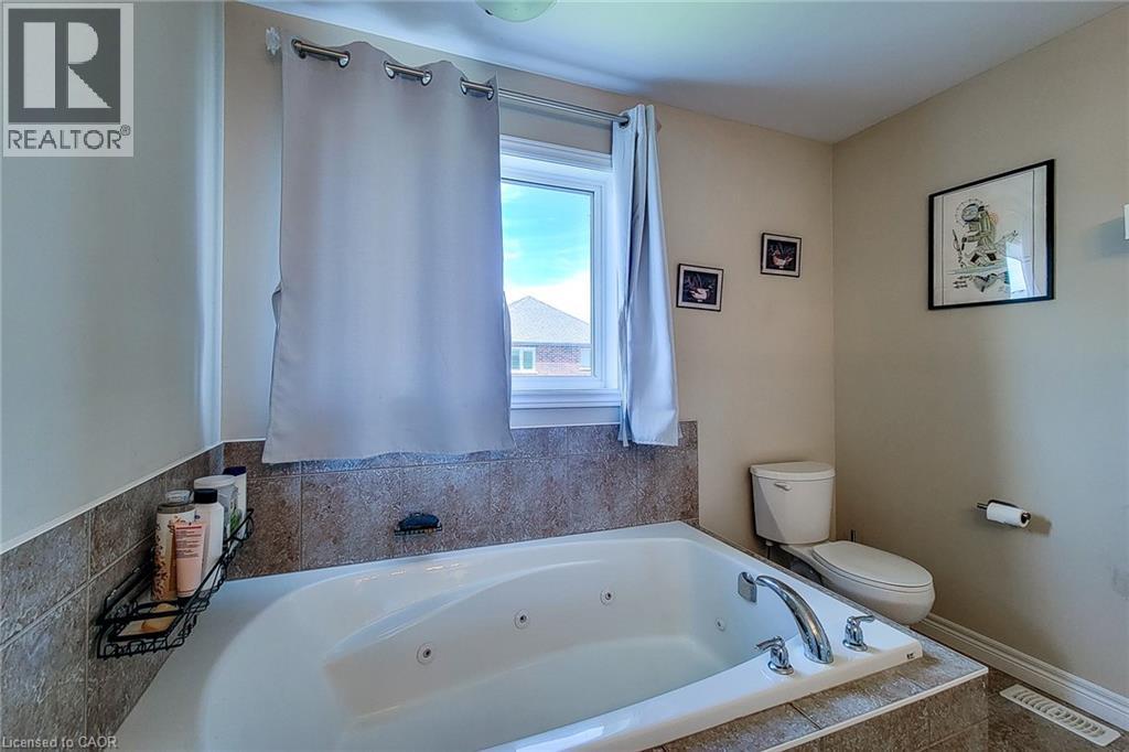 Built-in soaking tub with chrome fixtures, surrounded by neutral-toned tiled walls and flooring - 40 Fairgrounds Drive, Binbrook, ON - Indoor Photo Showing Bathroom