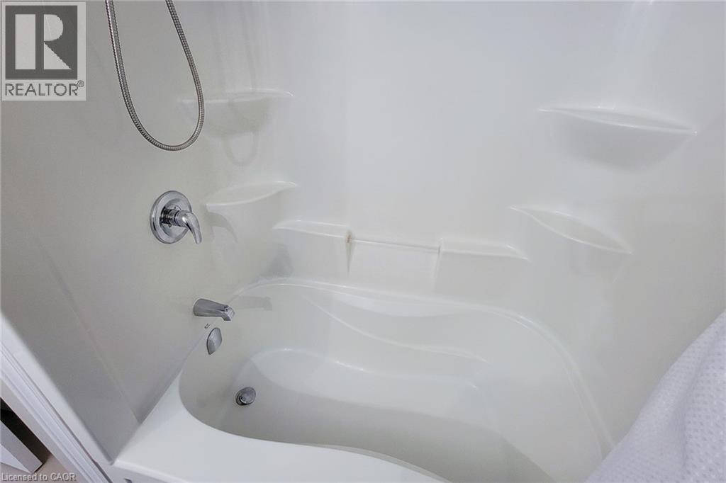 White fiberglass shower and tub combination featuring built-in shelving, a curved tub basin, and chrome fixtures - 40 Fairgrounds Drive, Binbrook, ON - Indoor Photo Showing Bathroom