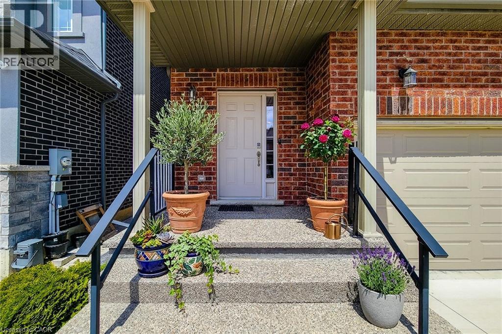 Inviting front entrance featuring a white panel door, exposed aggregate steps, and black metal handrails - 40 Fairgrounds Drive, Binbrook, ON - Outdoor With Deck Patio Veranda With Exterior