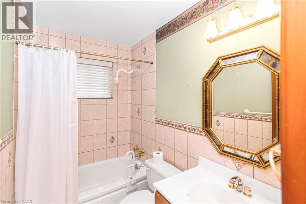 Bathroom featuring a combination tub/shower with tiled surround, a vanity with an integrated sink, an octagonal mirror, and wall-mounted light fixture - 435 East 36Th Street, Hamilton, ON - Indoor Photo Showing Bathroom