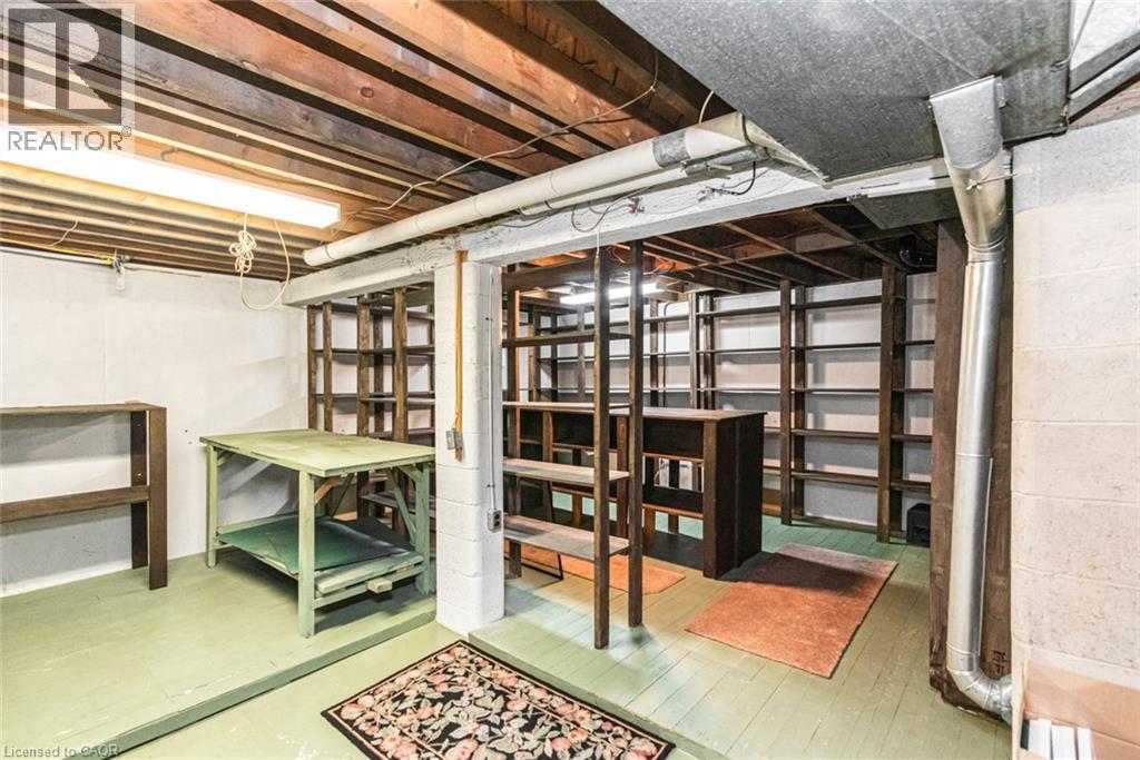 Lower level utility space featuring painted flooring, exposed ceiling joists, white-painted concrete block walls, overhead fluorescent lighting, and extensive built-in shelving units - 435 East 36Th Street, Hamilton, ON - Indoor Photo Showing Basement