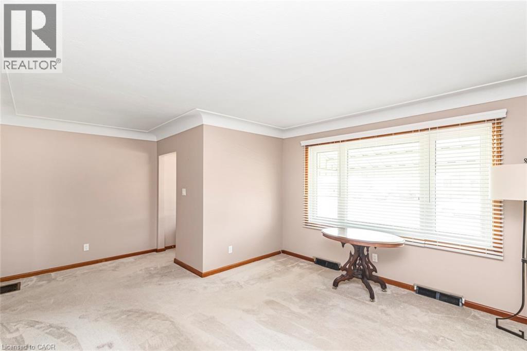Spacious room featuring neutral wall tones, light-colored carpeting, a large window with blinds, and white crown molding - 435 East 36Th Street, Hamilton, ON - Indoor