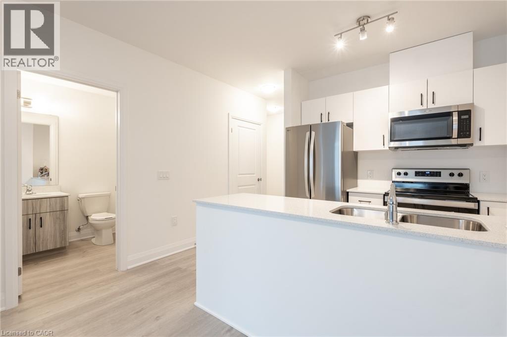 Modern kitchen featuring white cabinetry, stainless steel appliances, and a double basin sink set within a light-colored countertop - 1936 Rymal Road E Unit# 512, Hamilton, ON - Indoor Photo Showing Kitchen With Stainless Steel Kitchen