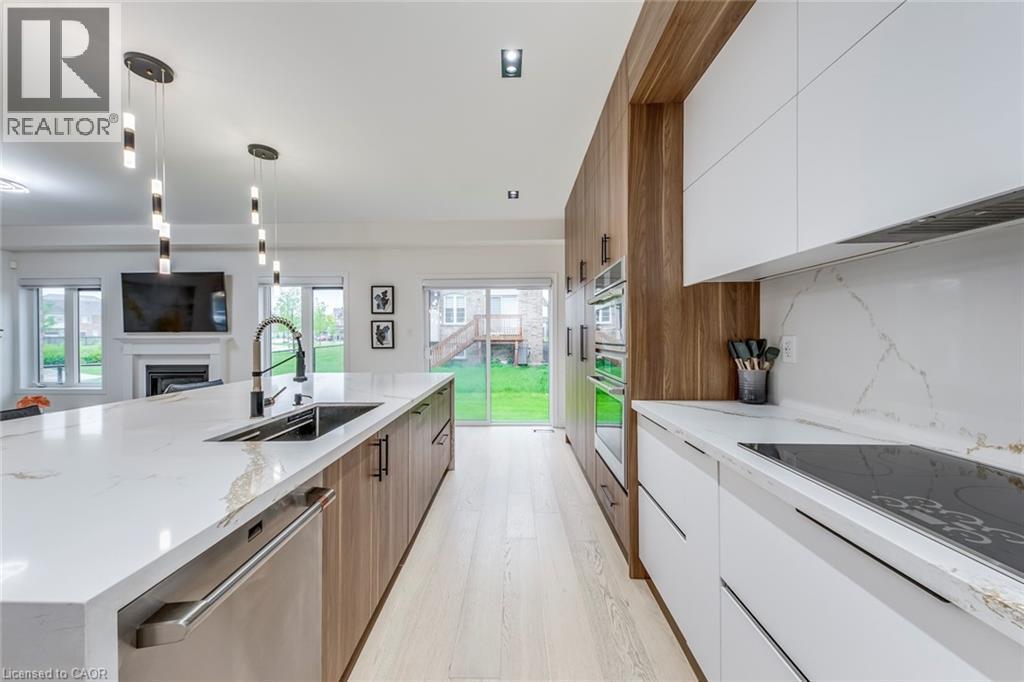 Contemporary kitchen featuring a large center island with integrated sink, sleek white and wood-finish cabinetry, built-in stainless steel appliances, and light wood-finish flooring - 3937 Leonardo Street, Burlington, ON - Indoor Photo Showing Kitchen