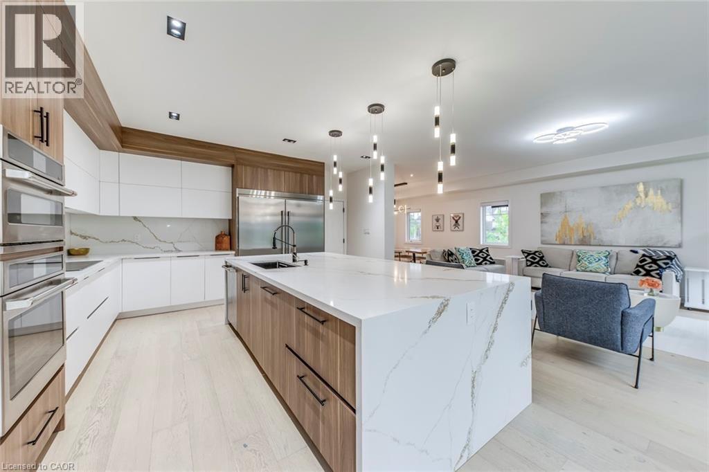 Open-concept kitchen featuring an expansive island with a waterfall countertop, integrated stainless steel appliances, wood-finish and white cabinetry, recessed lighting, and wood-finish flooring - 3937 Leonardo Street, Burlington, ON - Indoor Photo Showing Kitchen With Upgraded Kitchen