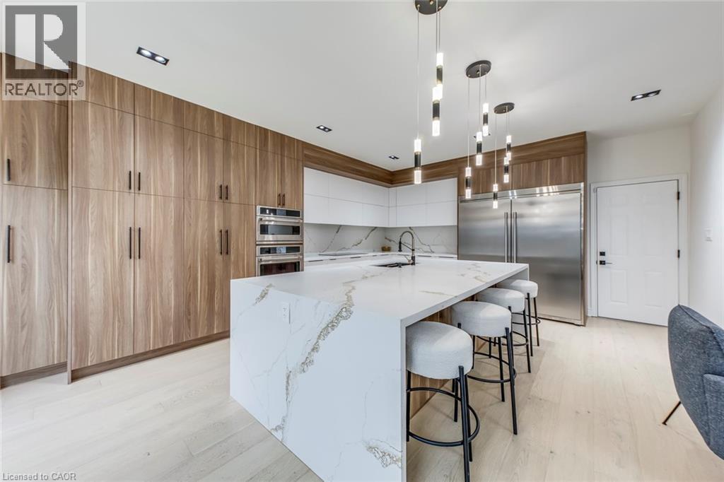 Gourmet kitchen featuring a waterfall island with a quartz countertop, integrated sink with a matte black faucet, full-height wood-finish cabinetry, and stainless steel built-in appliances - 3937 Leonardo Street, Burlington, ON - Indoor Photo Showing Kitchen With Upgraded Kitchen