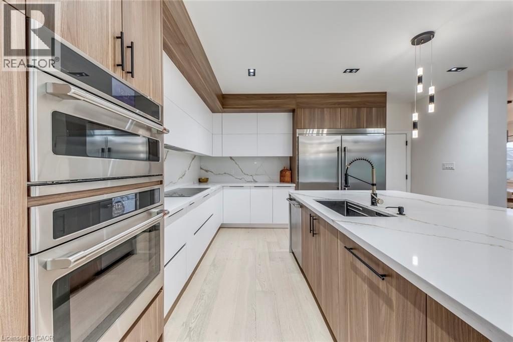 Modern kitchen featuring light wood-finish and white cabinetry, integrated stainless steel appliances, a large center island with an undermount sink, and light-toned flooring - 3937 Leonardo Street, Burlington, ON - Indoor Photo Showing Kitchen With Upgraded Kitchen