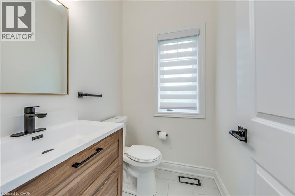 Bathroom featuring a wood-finish vanity with a white countertop and integrated sink, matte black hardware, a toilet, a window with horizontal blinds, and tile flooring - 3937 Leonardo Street, Burlington, ON - Indoor Photo Showing Bathroom