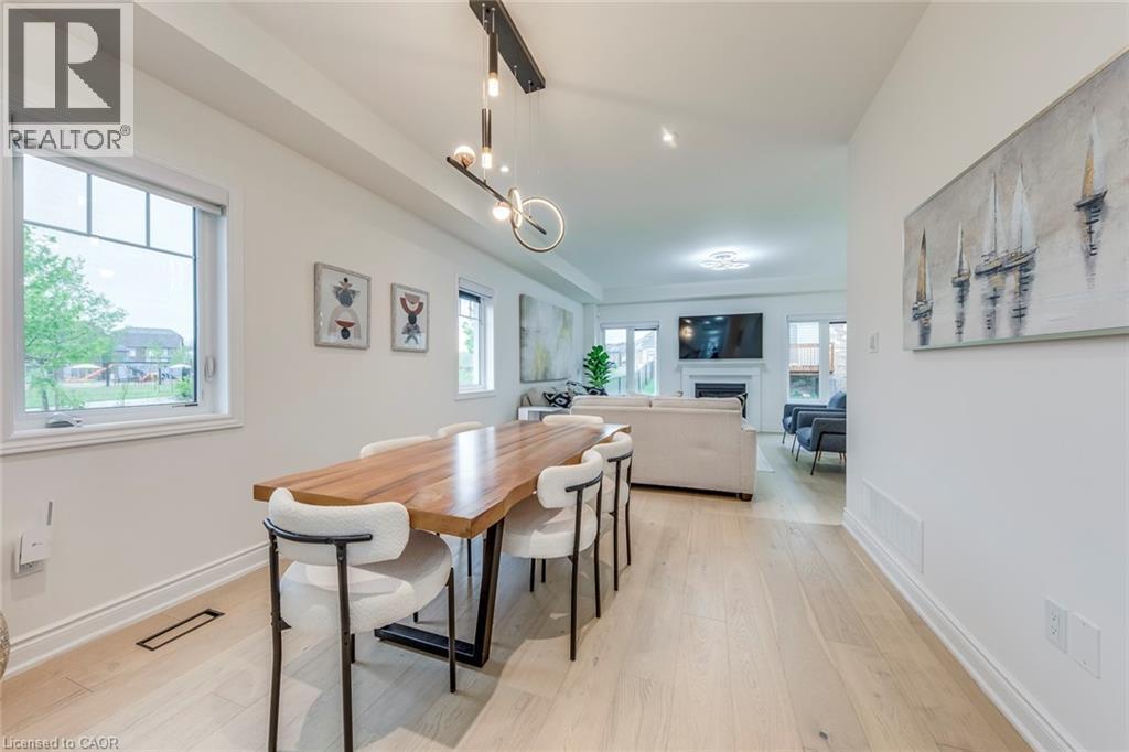 Open-concept dining area featuring light wood-finish flooring, a contemporary linear chandelier, and ample natural light from multiple windows - 3937 Leonardo Street, Burlington, ON - Indoor Photo Showing Dining Room
