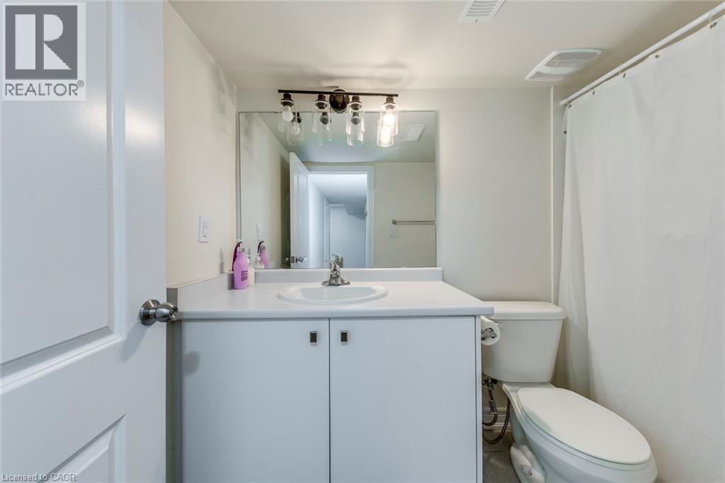 Bathroom featuring a white vanity with integrated sink, chrome faucet, a wall-mounted mirror, and industrial-style vanity lighting - 3937 Leonardo Street, Burlington, ON - Indoor Photo Showing Bathroom