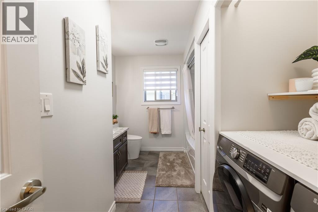 Compact laundry area featuring a front-loading washing machine, countertop space, and floating shelf - 10 Redbud Crescent, Simcoe, ON - Indoor Photo Showing Laundry Room