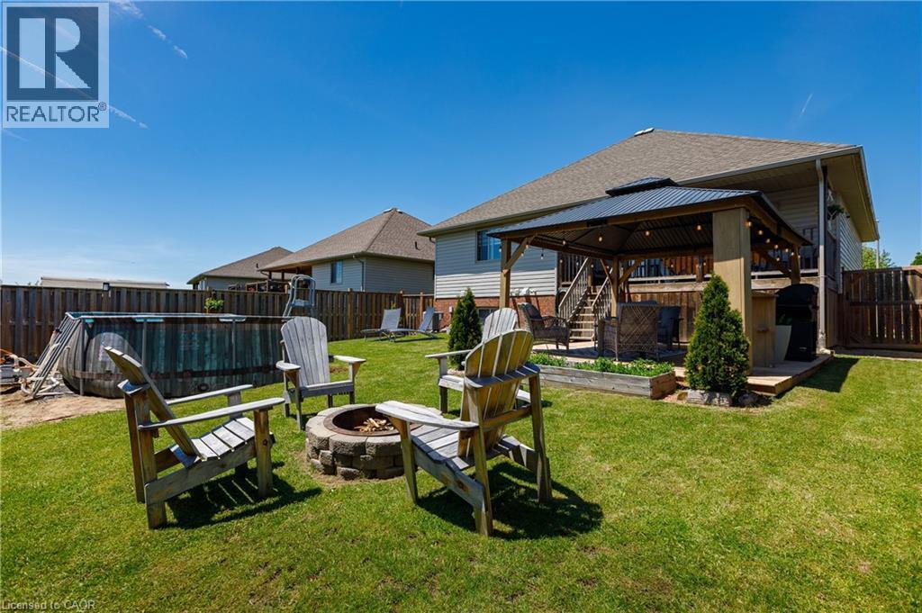 Expansive backyard featuring a stone-ringed fire pit, a covered patio with string lighting, and a terraced wooden deck - 10 Redbud Crescent, Simcoe, ON - Outdoor