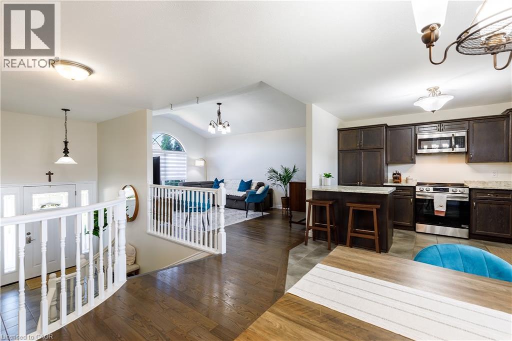 Open-concept design featuring wood-finish flooring, a kitchen island with seating, dark wood cabinetry, and stainless steel appliances - 10 Redbud Crescent, Simcoe, ON - Indoor
