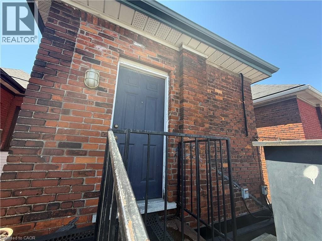 Brick exterior featuring a black entry door, metal handrail, and exterior lighting fixture - 359 Barton Street E Unit# Upper, Hamilton, ON - Outdoor With Exterior